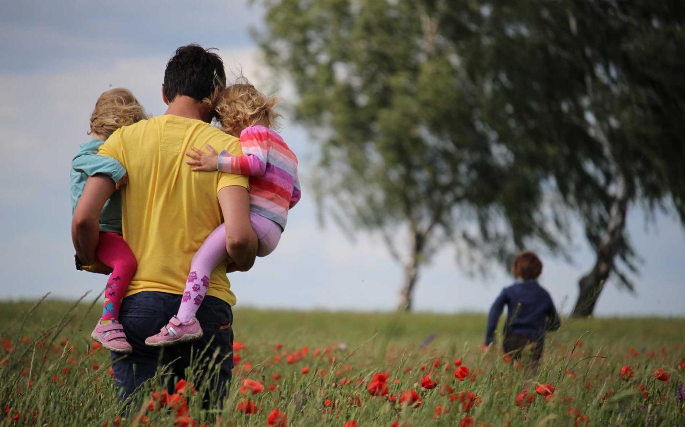 Dad holding children in field.